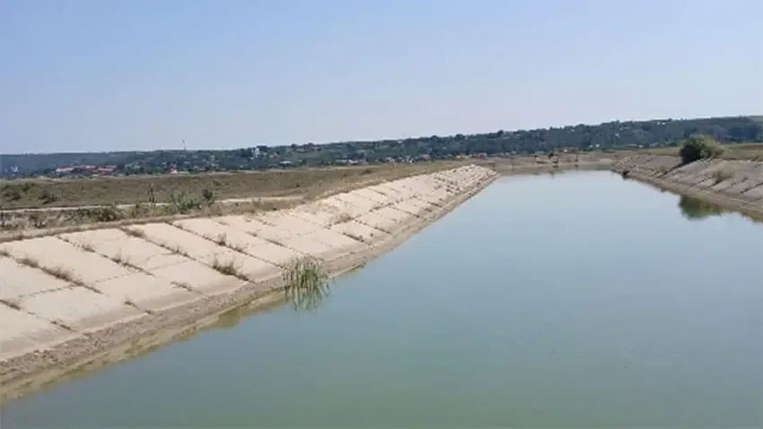 Canal de irigații betonat, cu apă, traversând un peisaj rural
