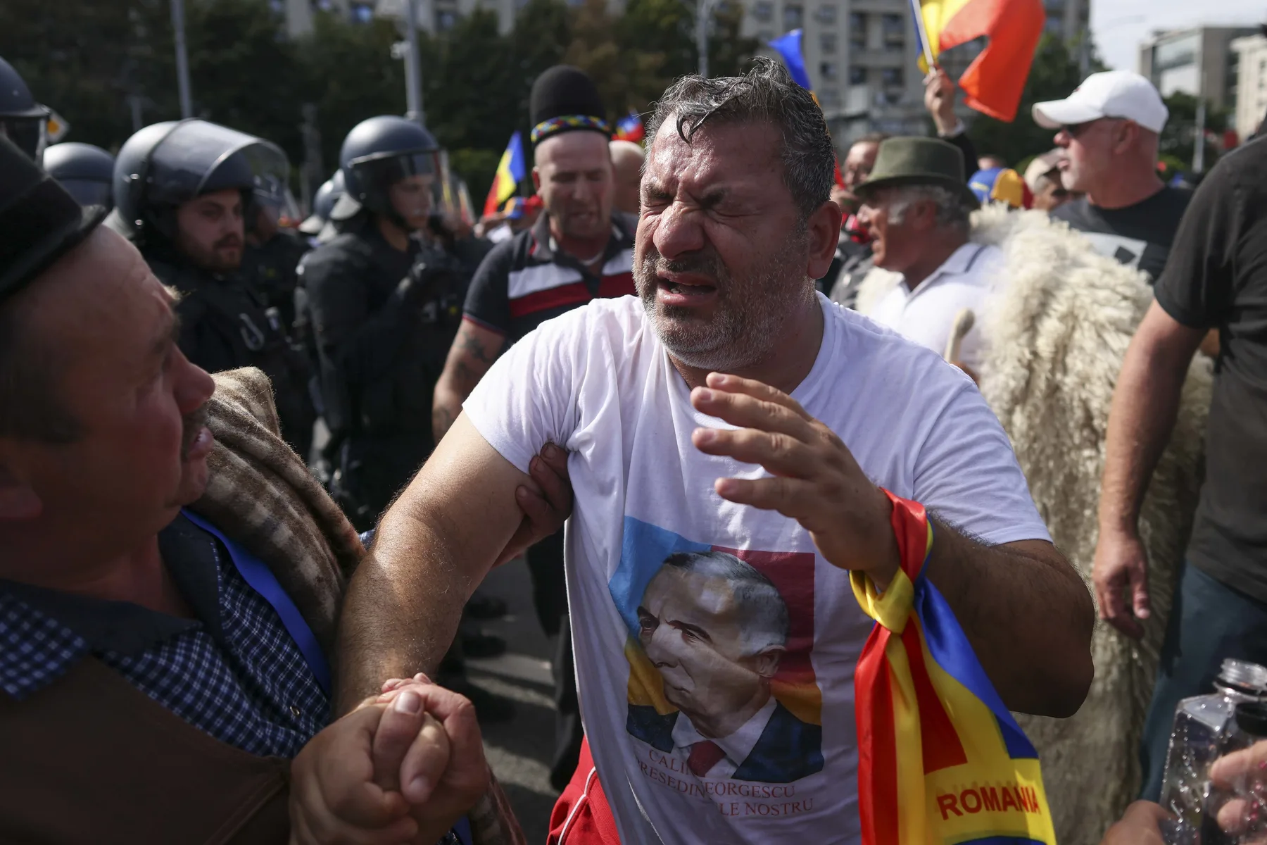Bărbat cu steag tricolor gesticulează în fața jandarmilor la protest