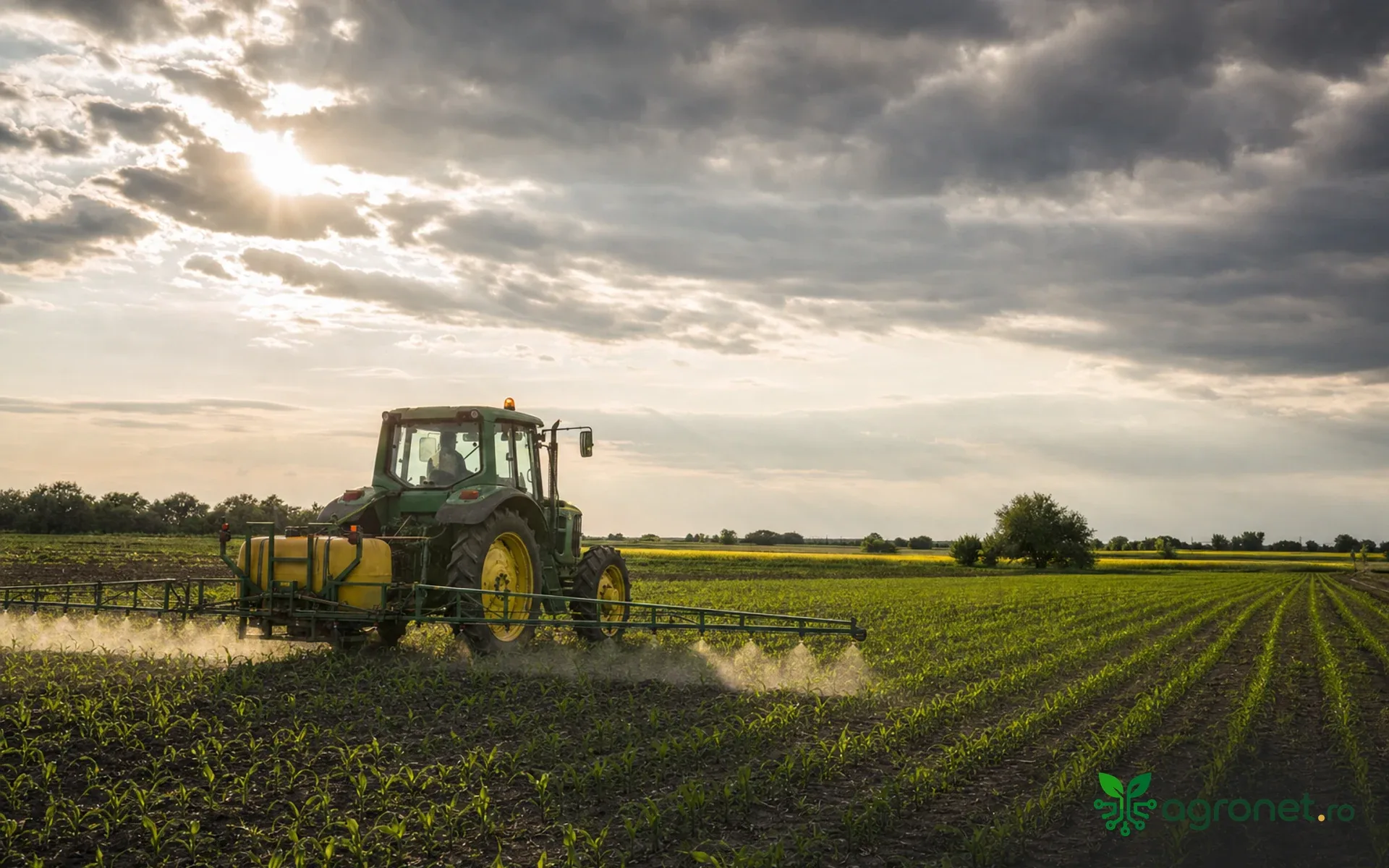 Peisaj agricol de vară, cu utilaje pregătite pentru o fereastră de lucru sub cer variabil