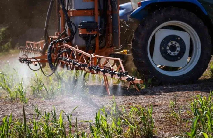 Tractor cu rampă de stropit aplică tratament pe o cultură tânără