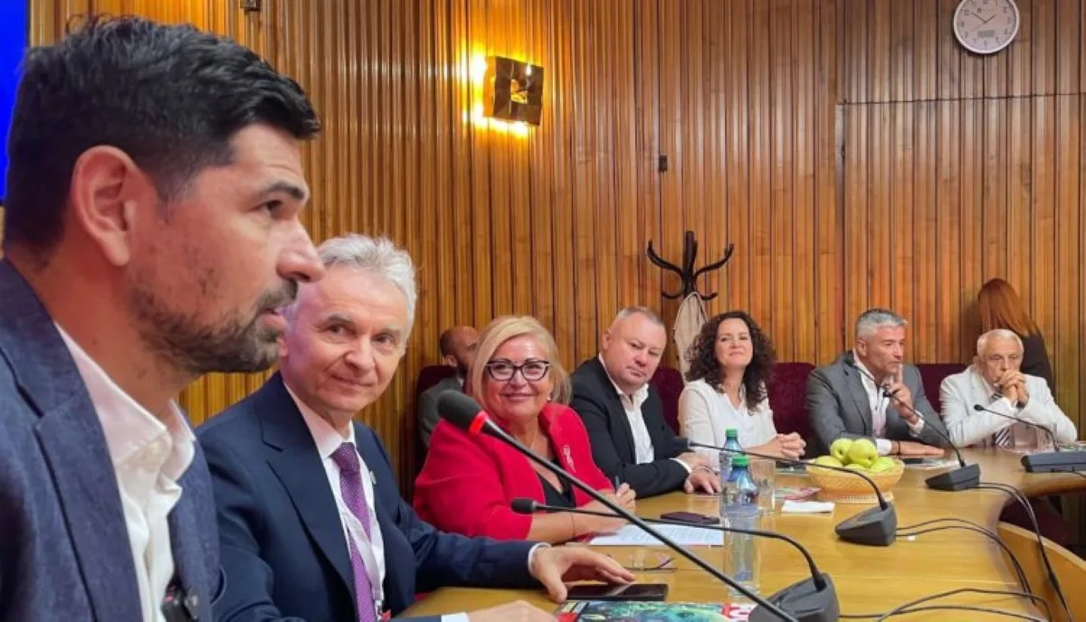 Vorbitori la masa de conferință, cu microfoane și materiale pe masă