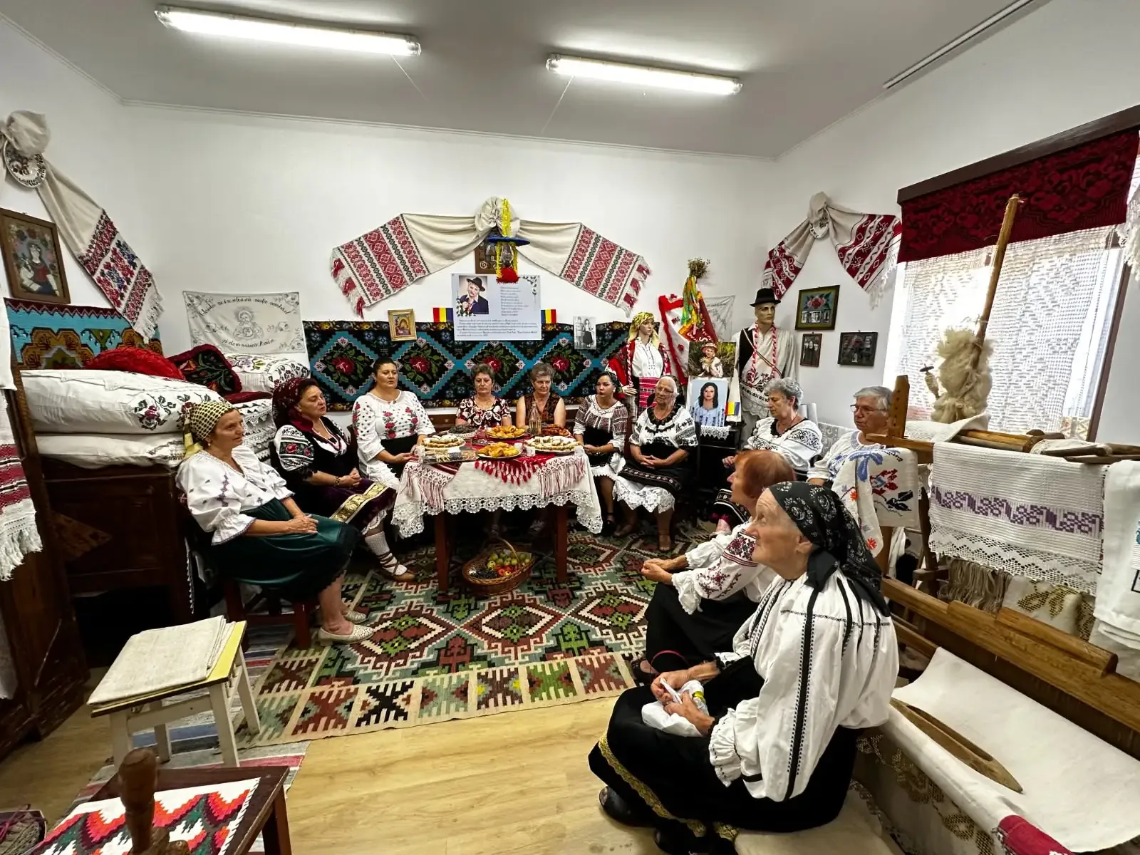 Grup în costume populare într-o cameră tradițională decorată cu țesături