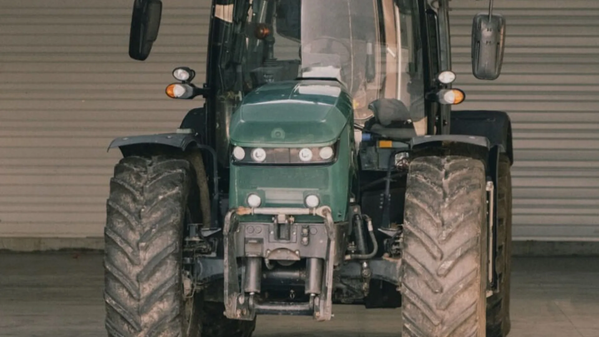 Tractor verde văzut din față, parcat într-un spațiu industrial