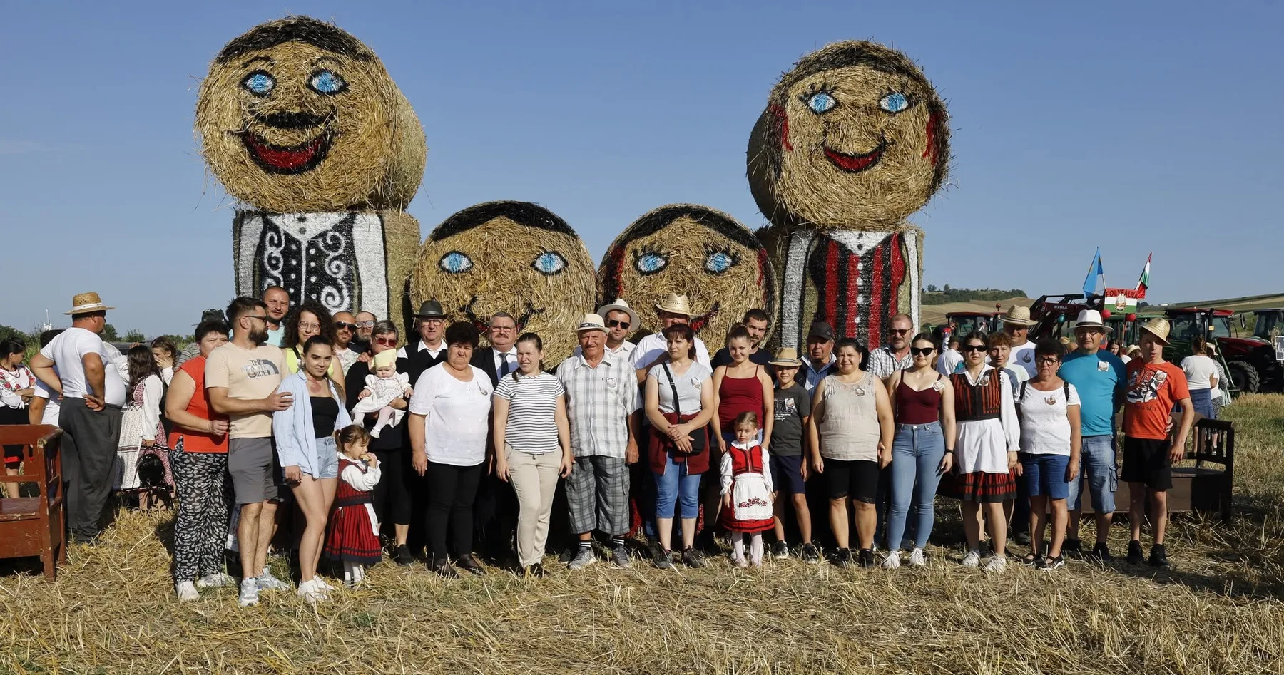 Grup de participanți în lan, lângă trei personaje uriașe din paie
