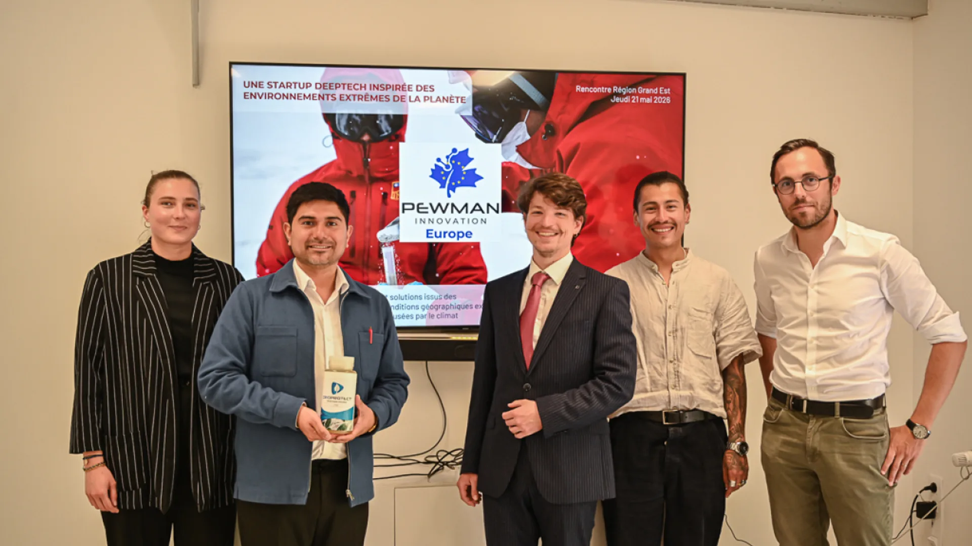 Cinci persoane stau într-o sală de prezentare, lângă un ecran cu sigla Pewman Innovation Europe, iar una ține un recipient de produs.