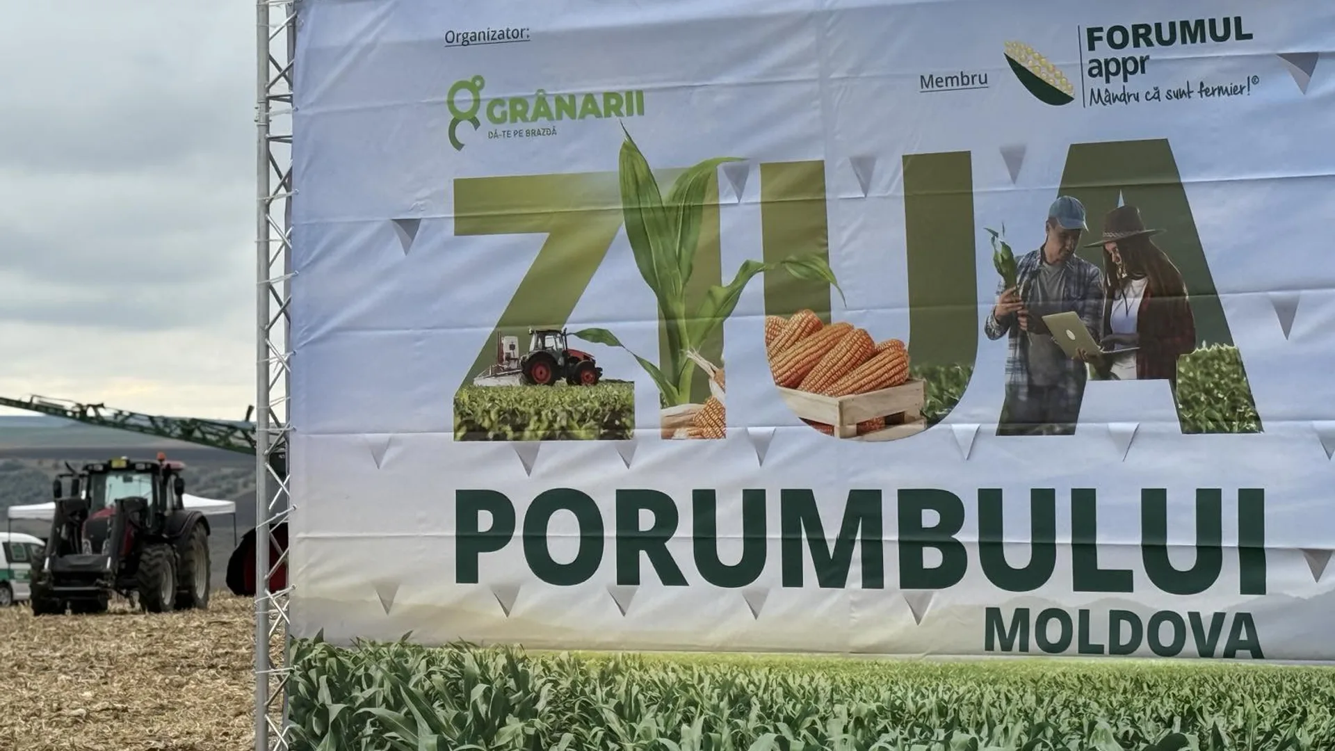Banner mare pentru un eveniment dedicat porumbului, amplasat la marginea unui câmp, cu un tractor vizibil în lateral.