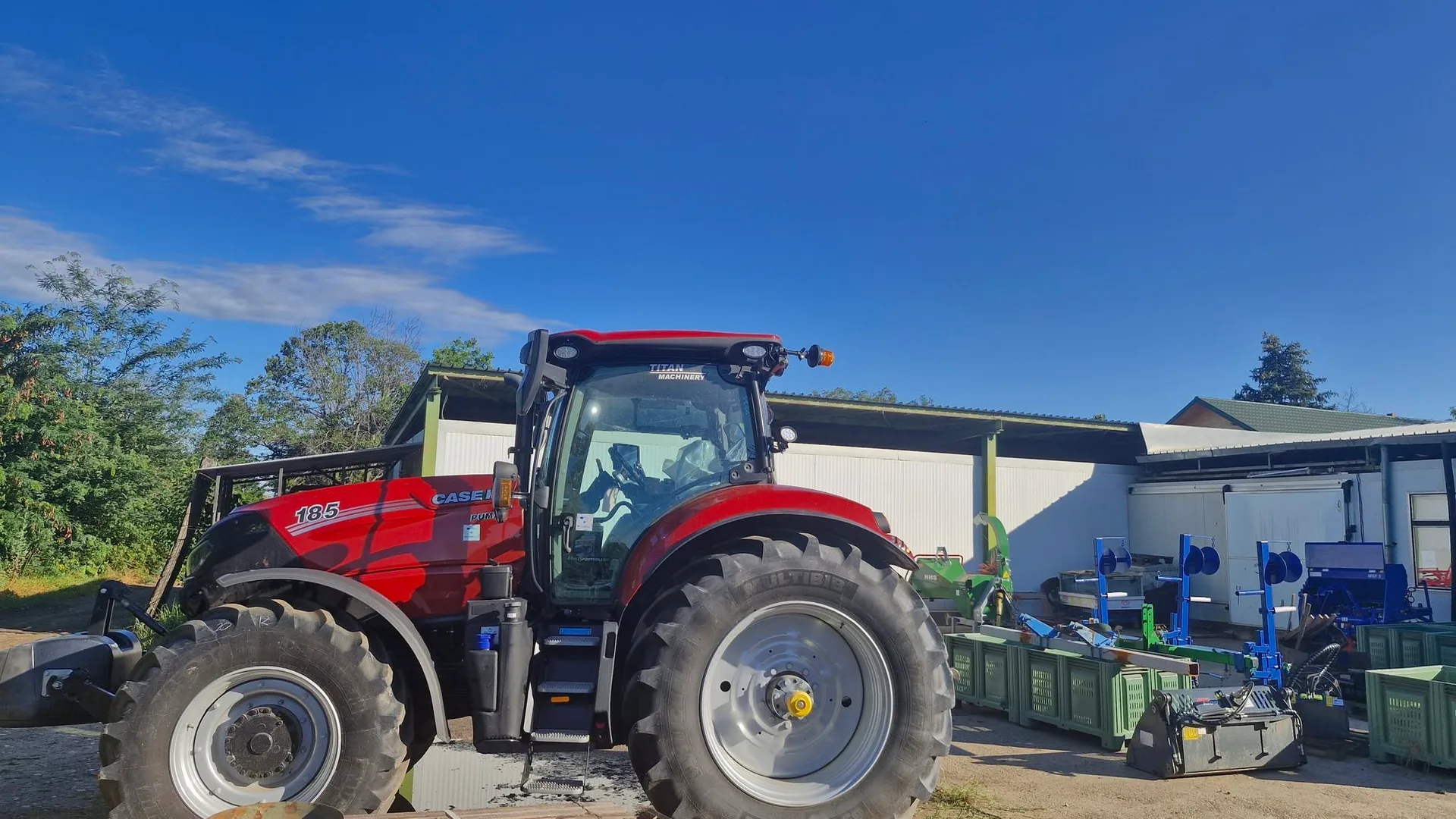 Tractor roșu cu utilaje agricole lângă containere și clădiri anexe