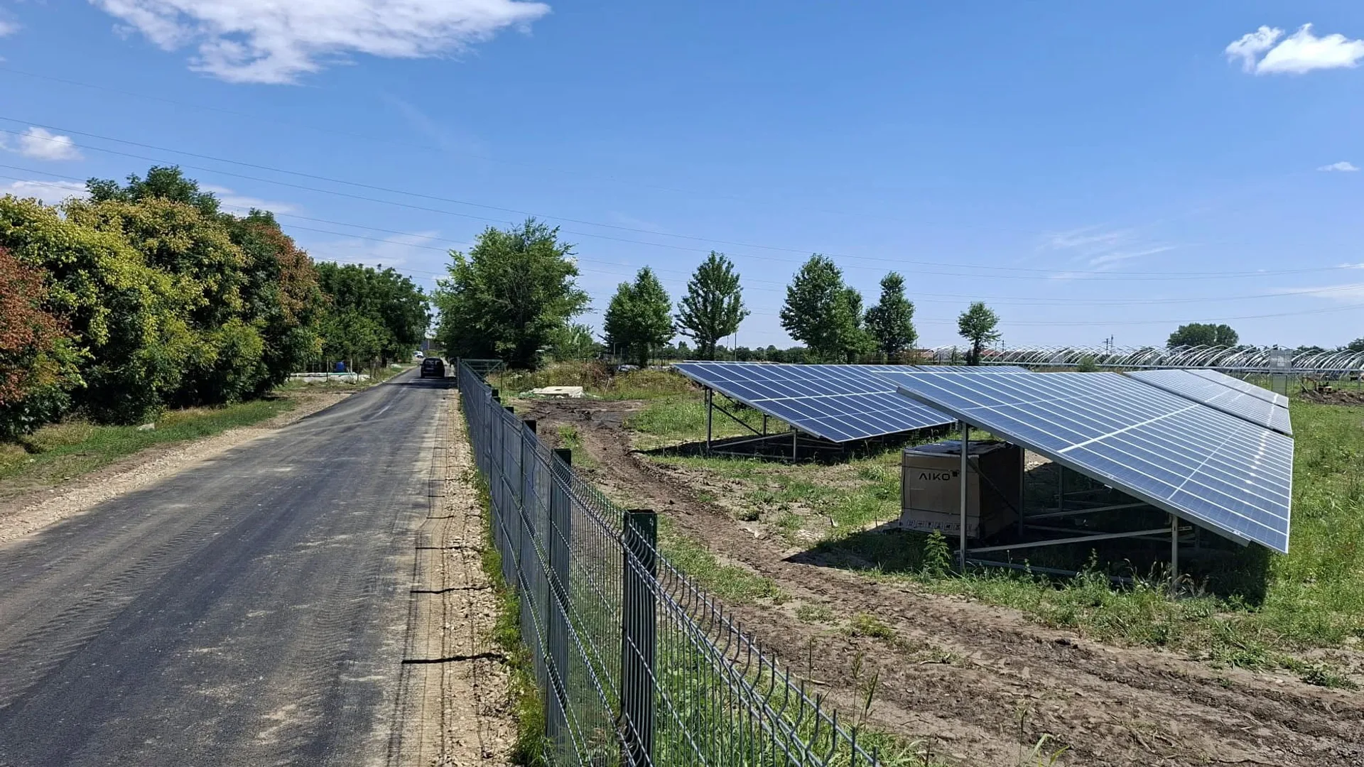 Panouri fotovoltaice instalate lângă drum, cu gard și arbori aliniați