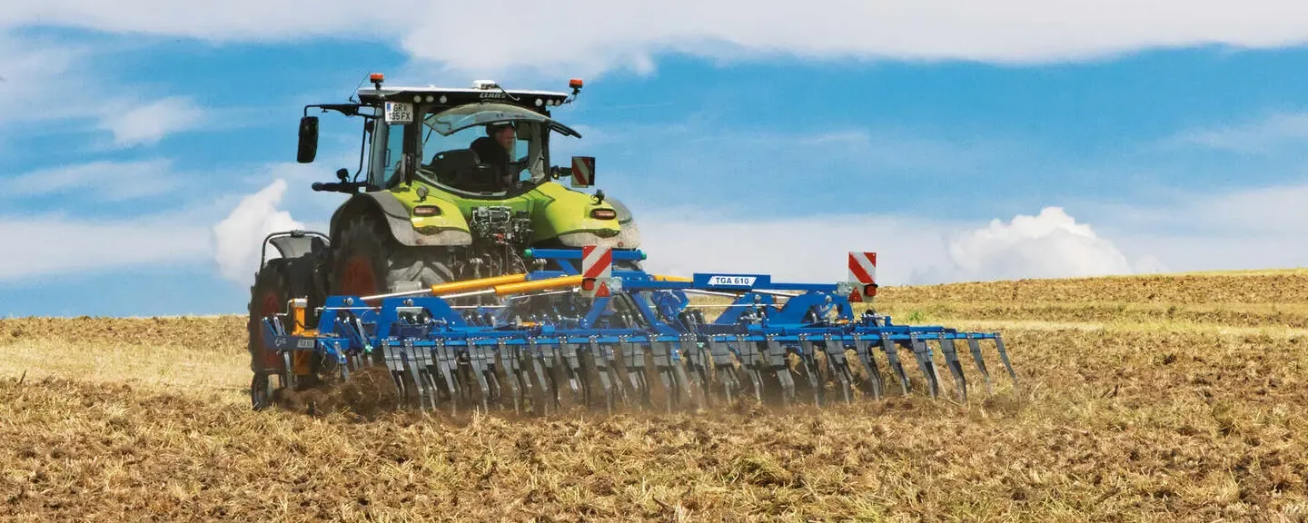 Tractor cu cultivator albastru lucrează superficial un câmp cu miriște