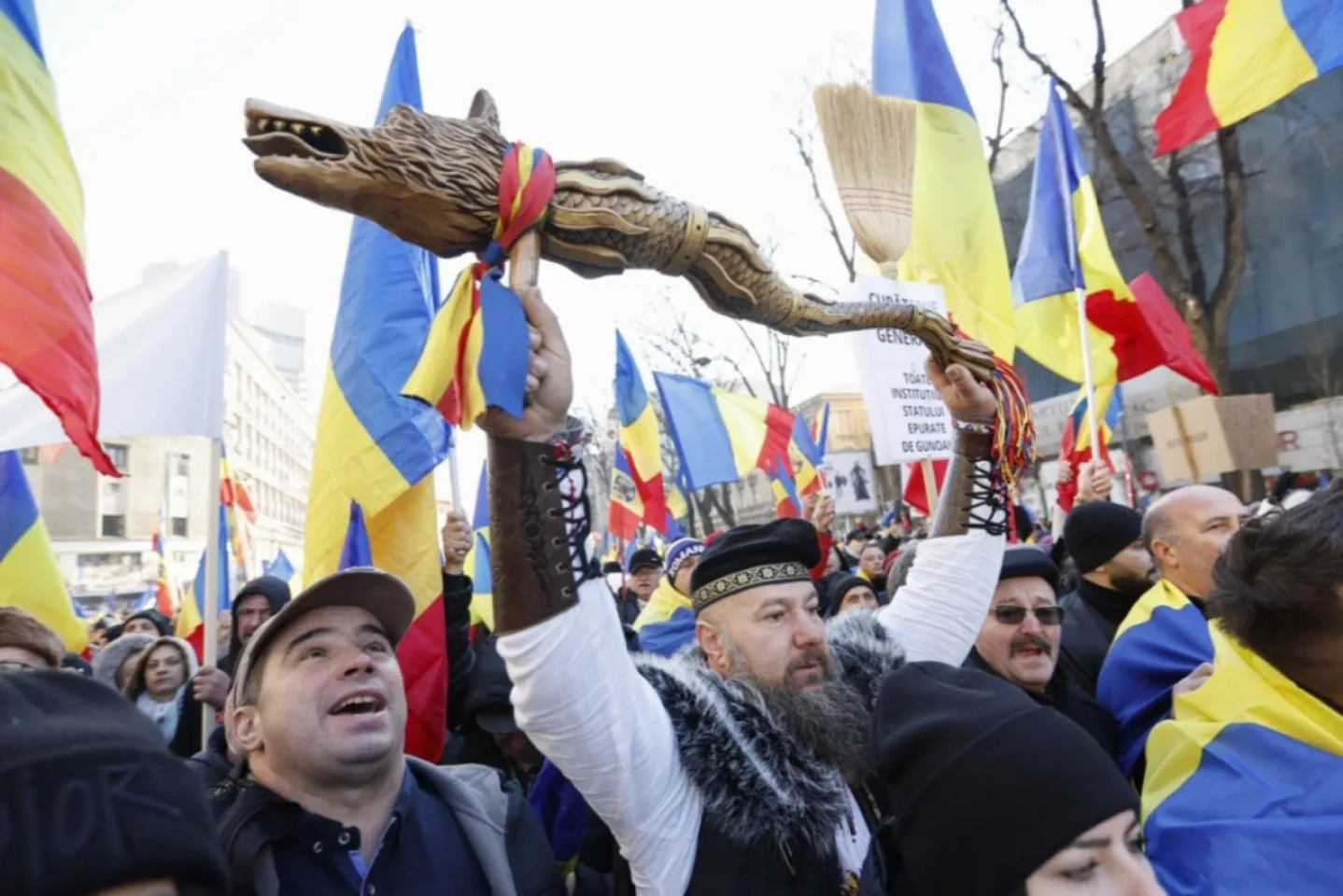 Manifestanți cu steaguri tricolore, unul ridicând un baston sculptat