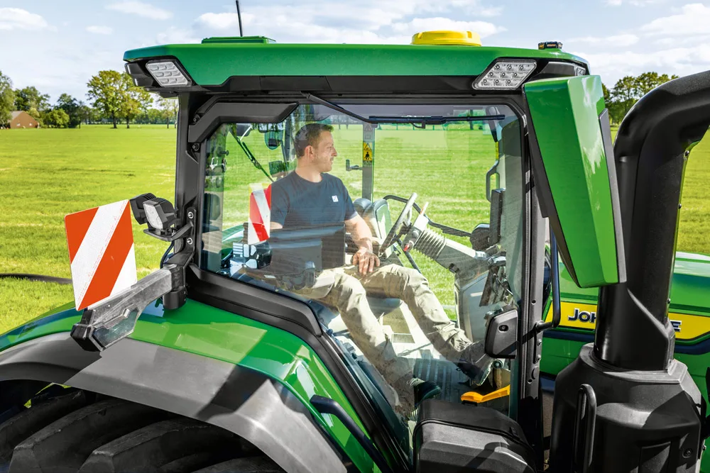 Cabina unui tractor John Deere, cu operatorul vizibil prin parbriz