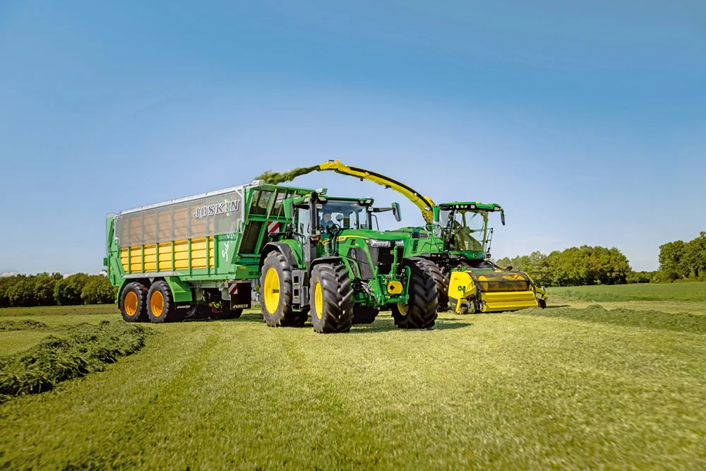 Tractor John Deere cosește iarbă și tractează o remorcă pe câmp