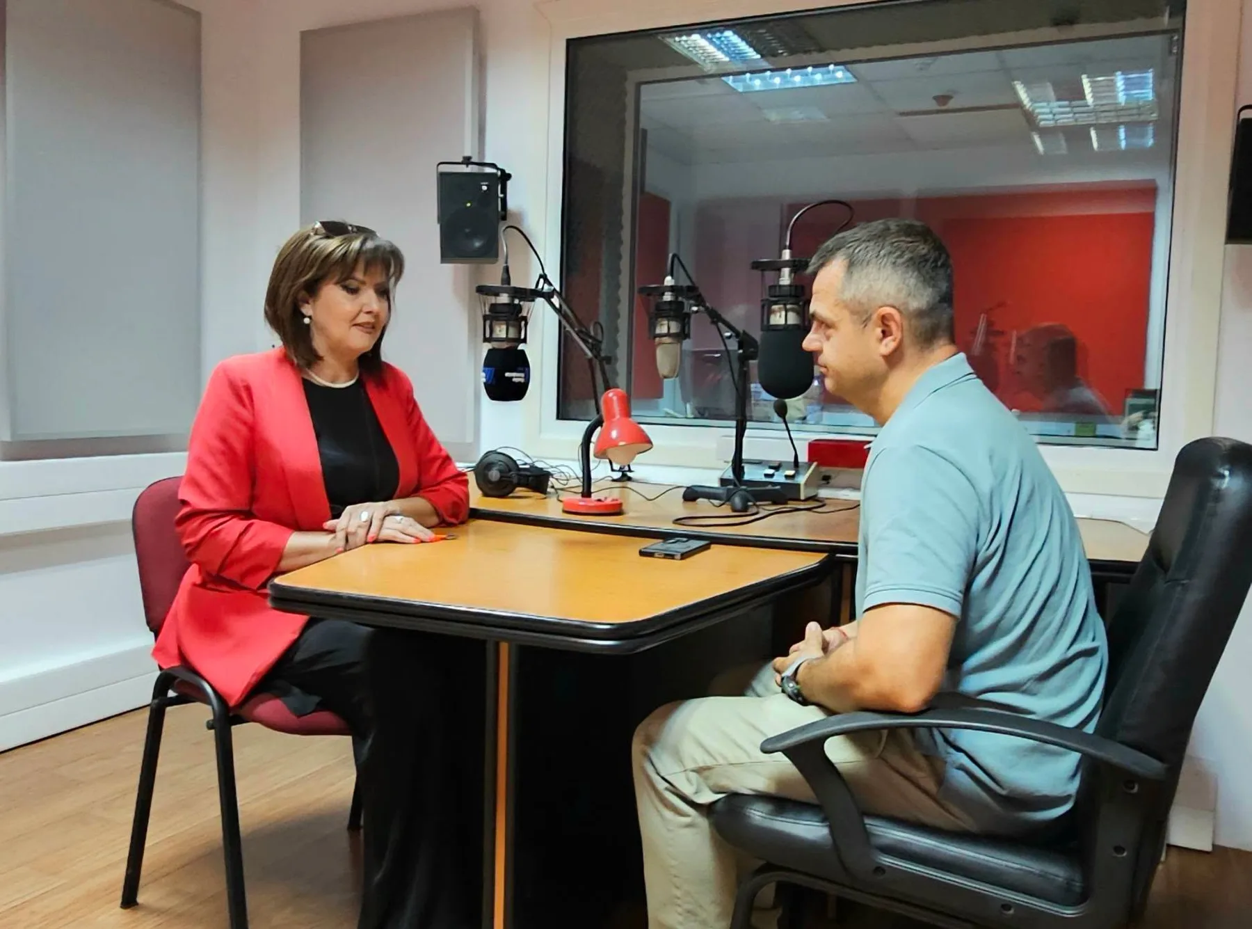 Doi interlocutori discută într-un studio radio, la masa cu microfoane