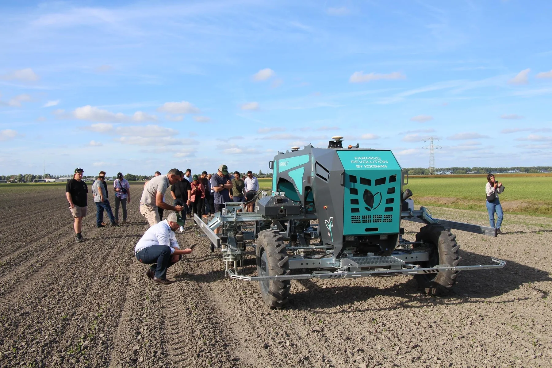 Robot agricol autonom pentru lucrări în câmp, inspectat de un grup de persoane pe un teren agricol.