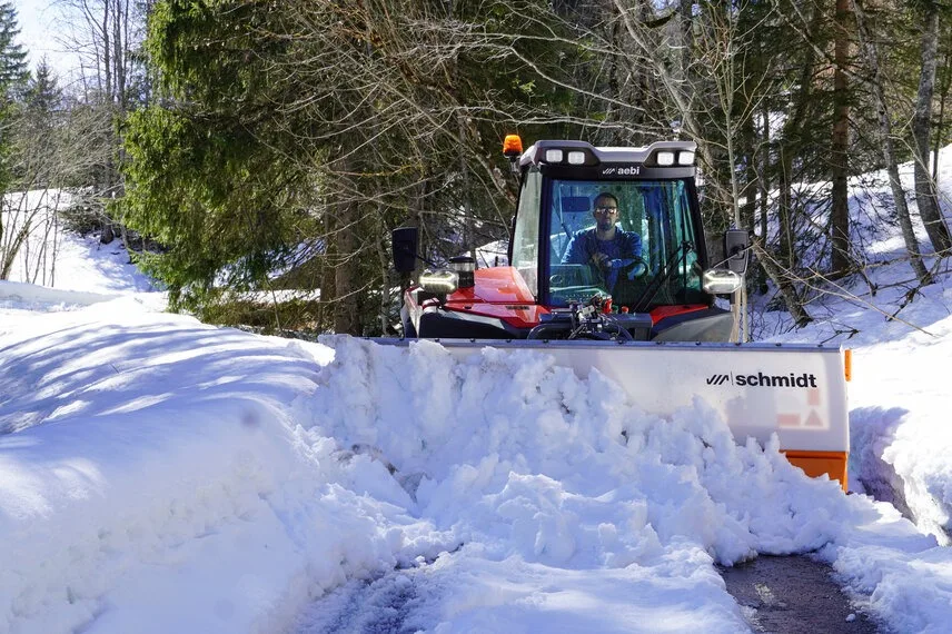 Utilaj compact deszăpezește un drum forestier îngust, printre troiene