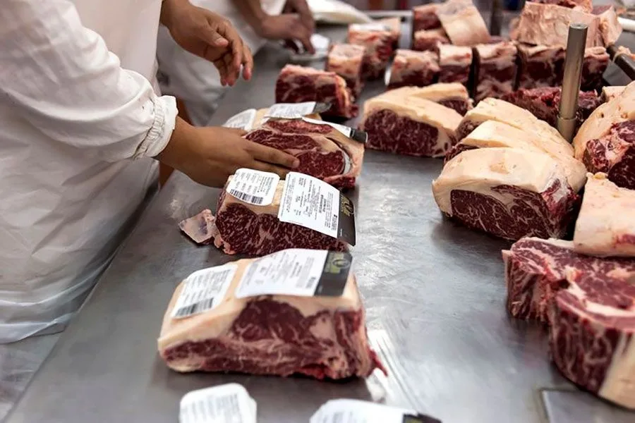 Bucăți de carne de vită refrigerată, etichetate, pe o masă metalică într-o unitate de procesare.
