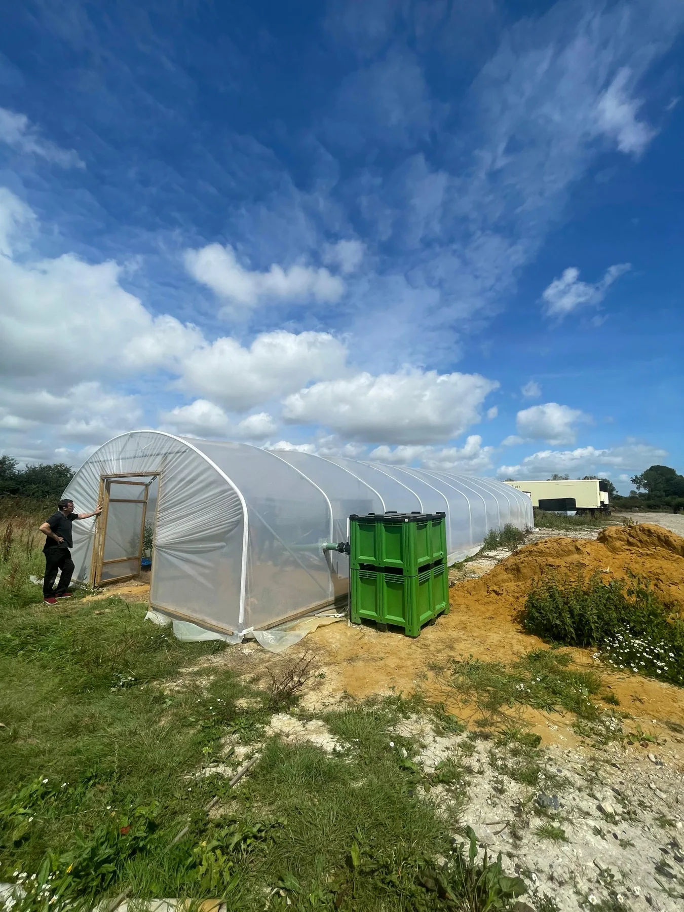 Tunel agricol din folie, cu container verde și o persoană la intrare