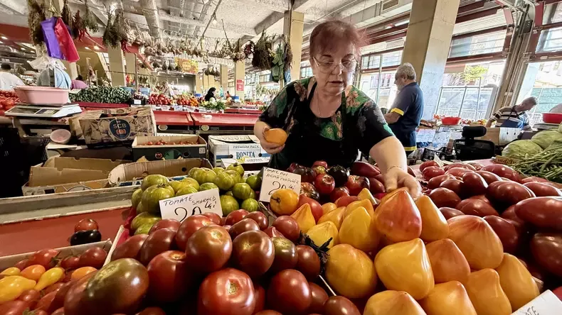 Vânzătoare aranjează roșii galbene, verzi și roșii pe tarabă