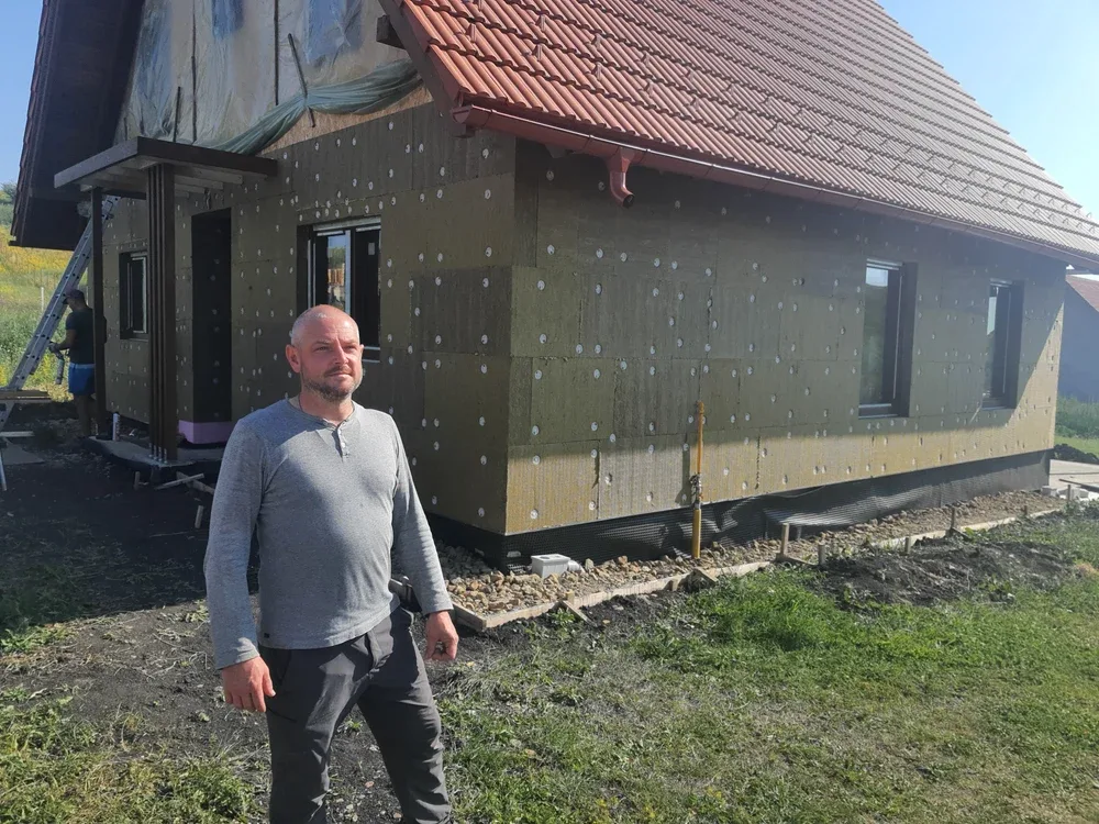 Bărbat lângă o casă în construcție, cu termoizolație montată pe fațadă