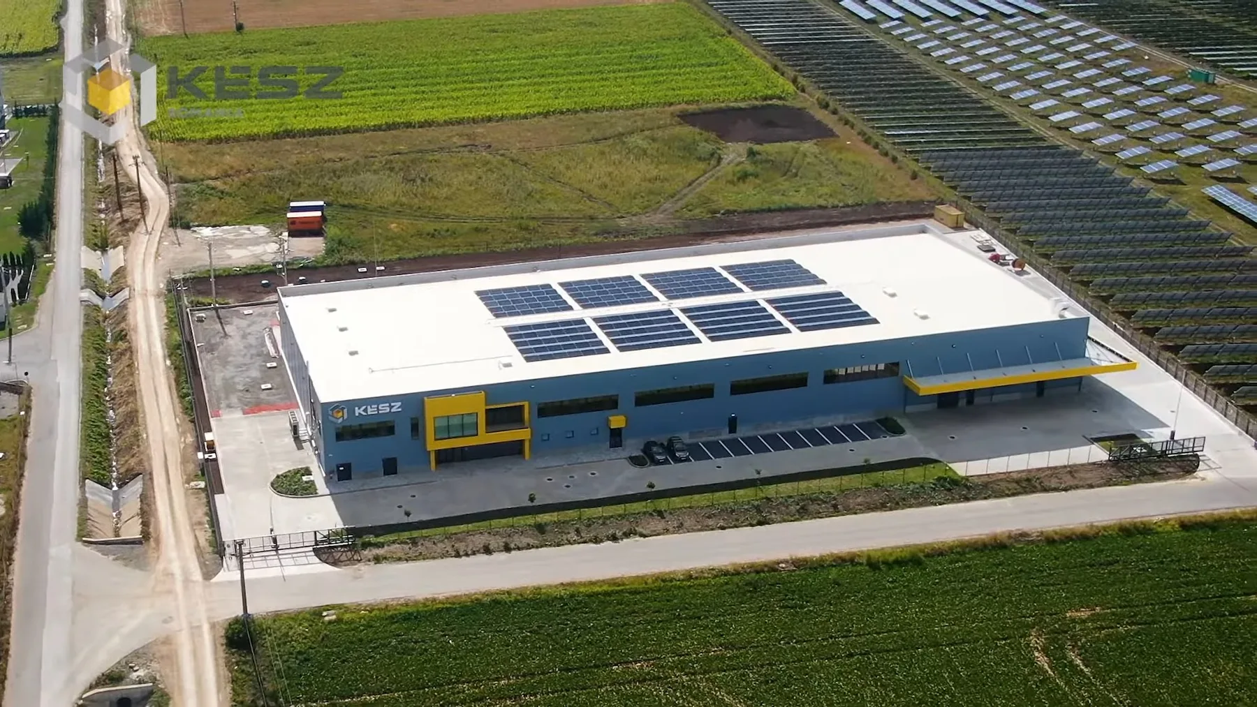 Hală industrială KÉSZ cu panouri fotovoltaice pe acoperiș, înconjurată de câmpuri