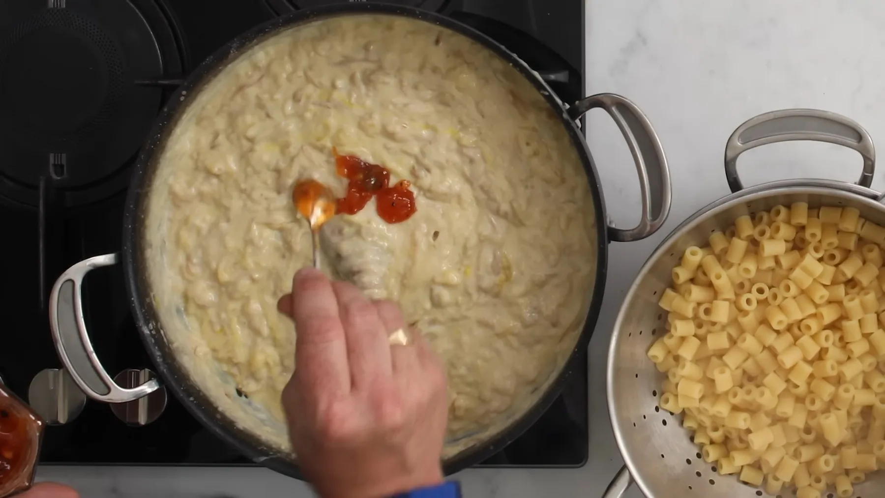 Condiment roșu adăugat cu lingura într-un sos cremos cu macaroane