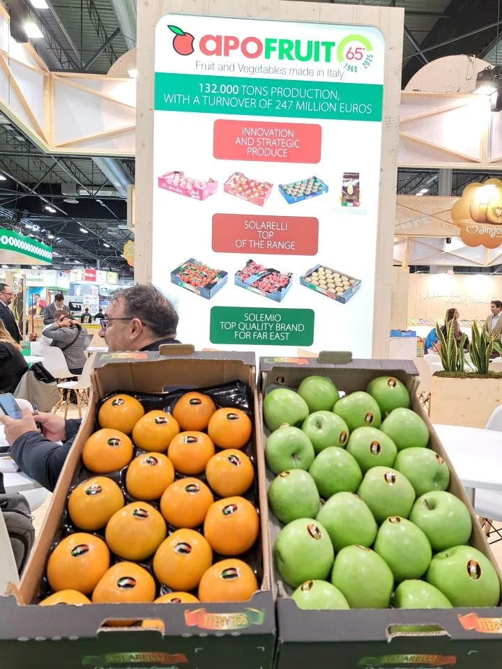 Stand Apofruit la târg, cu lăzi de fructe galbene și mere verzi