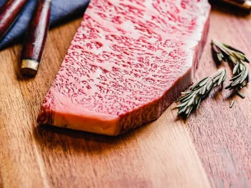 Bucată de vită crudă, intens marmorată, pe tocător de lemn