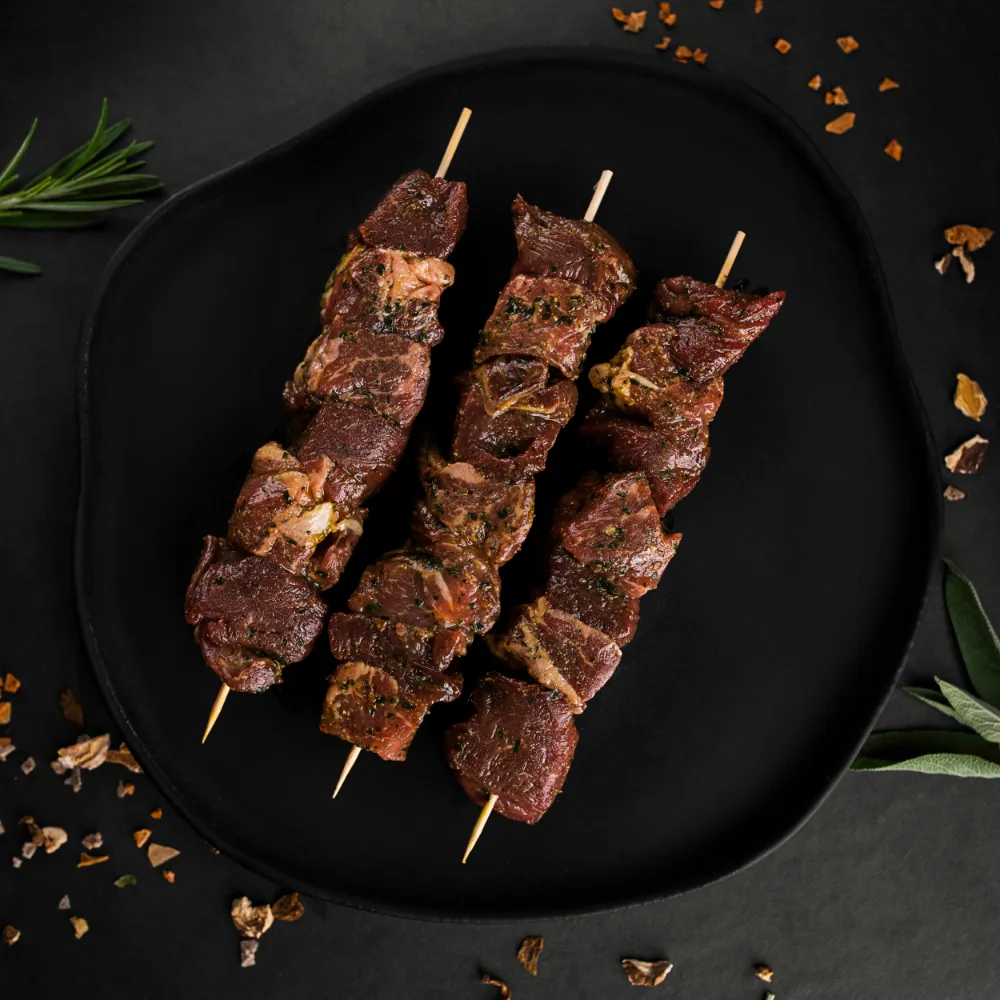 Frigărui de vită marinate, așezate pe farfurie neagră