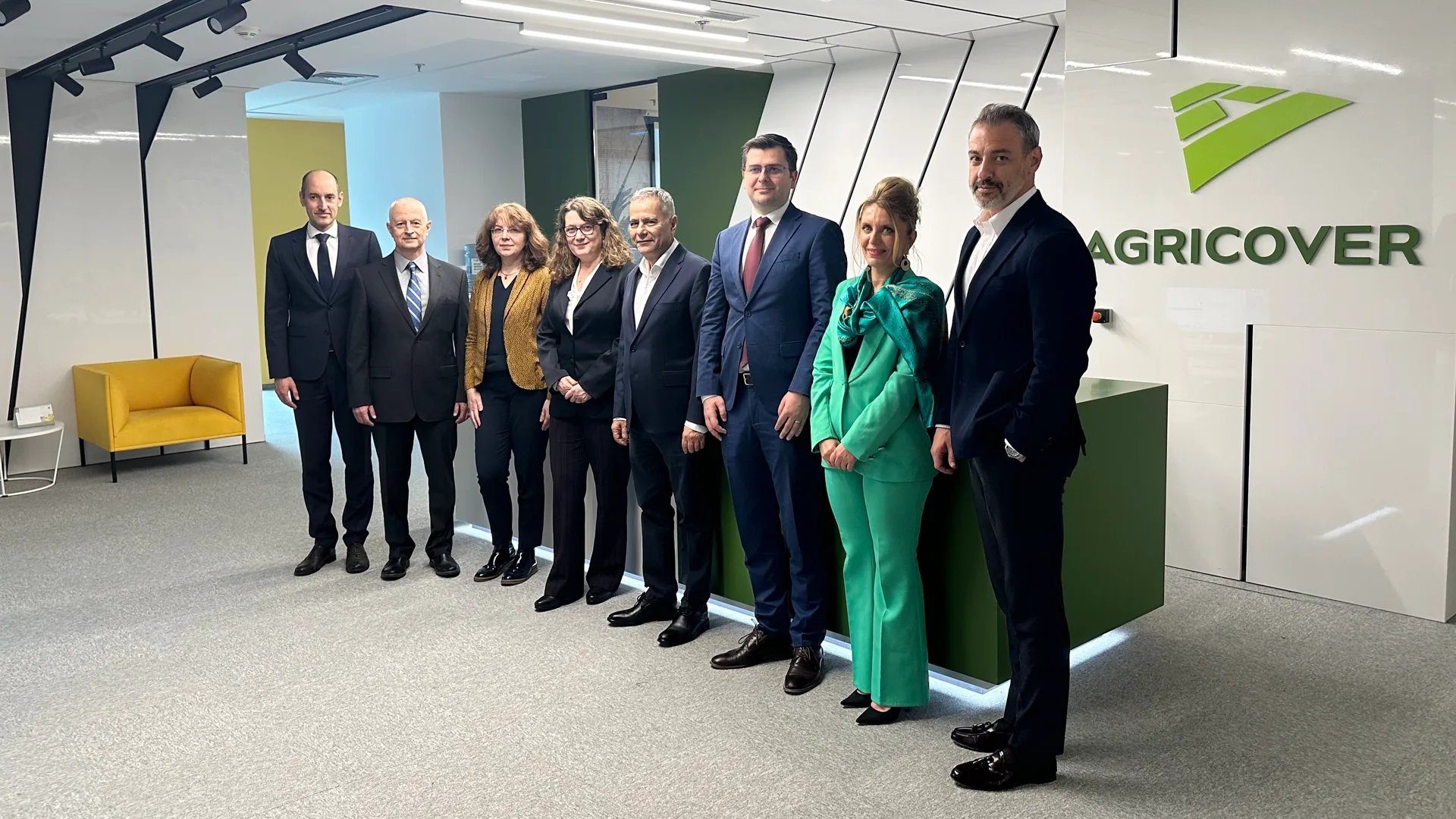 Grup de persoane în ținută business într-un birou, lângă recepția cu logo-ul Agricover.