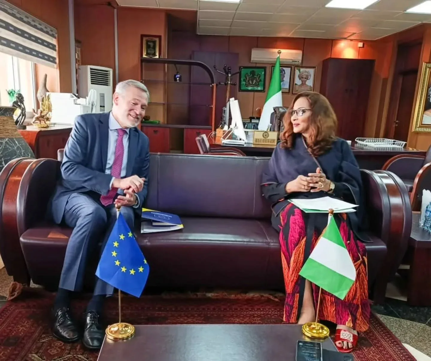 Doi oficiali discută într-un birou, lângă steagurile Uniunii Europene și Nigeriei