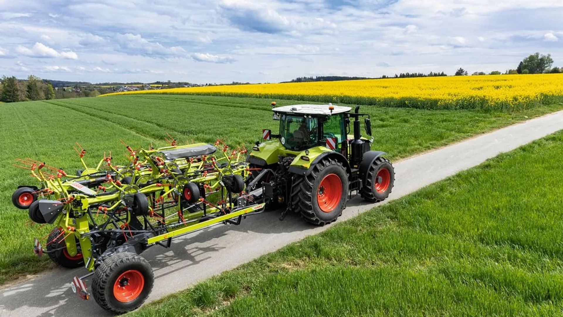 Tractor CLAAS transportă o greblă VOLTO pe drum între câmpuri