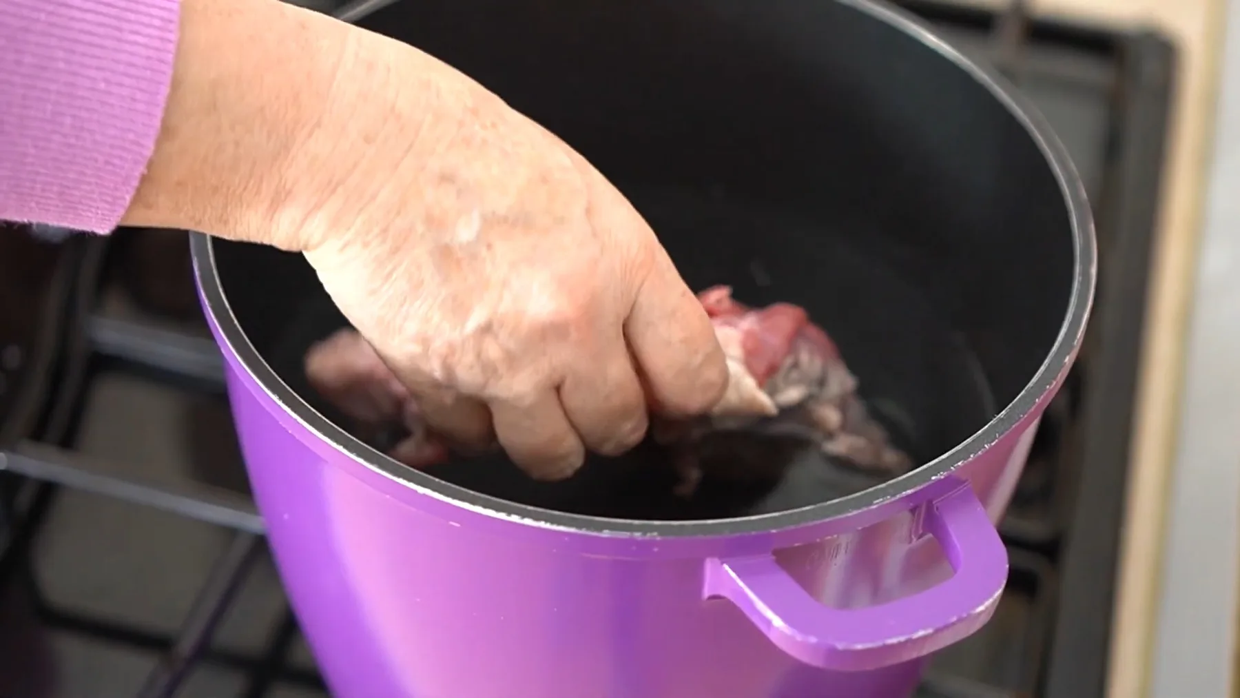 Mână așezând bucăți de carne de porc într-o oală mov