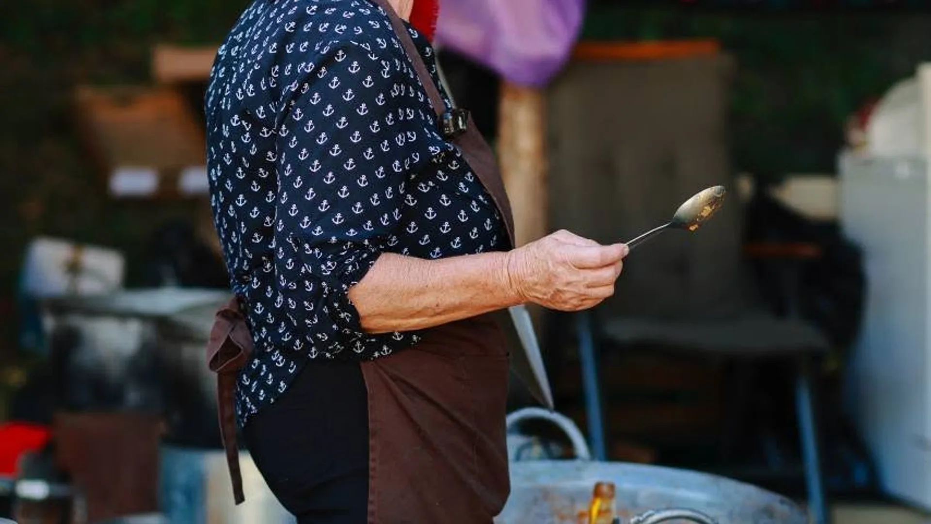Femeie cu șorț ține o lingură lângă zona de gătit