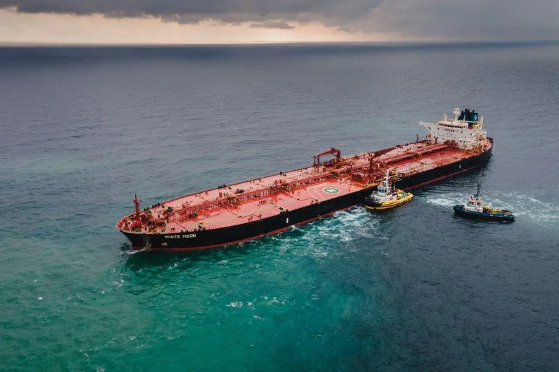 Petrolier escortat de remorchere pe mare, sub cer înnorat