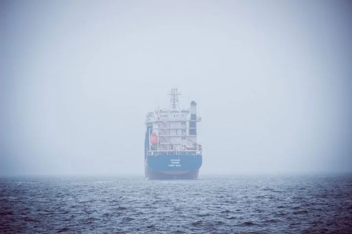 Navă cargo pe mare, abia vizibilă prin ceață densă