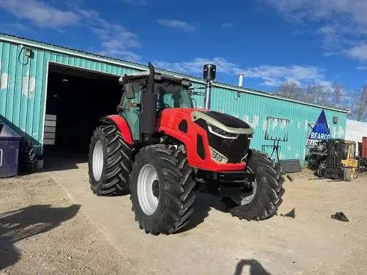 Tractor roșu pe platformă pietruită, lângă o hală metalică verde
