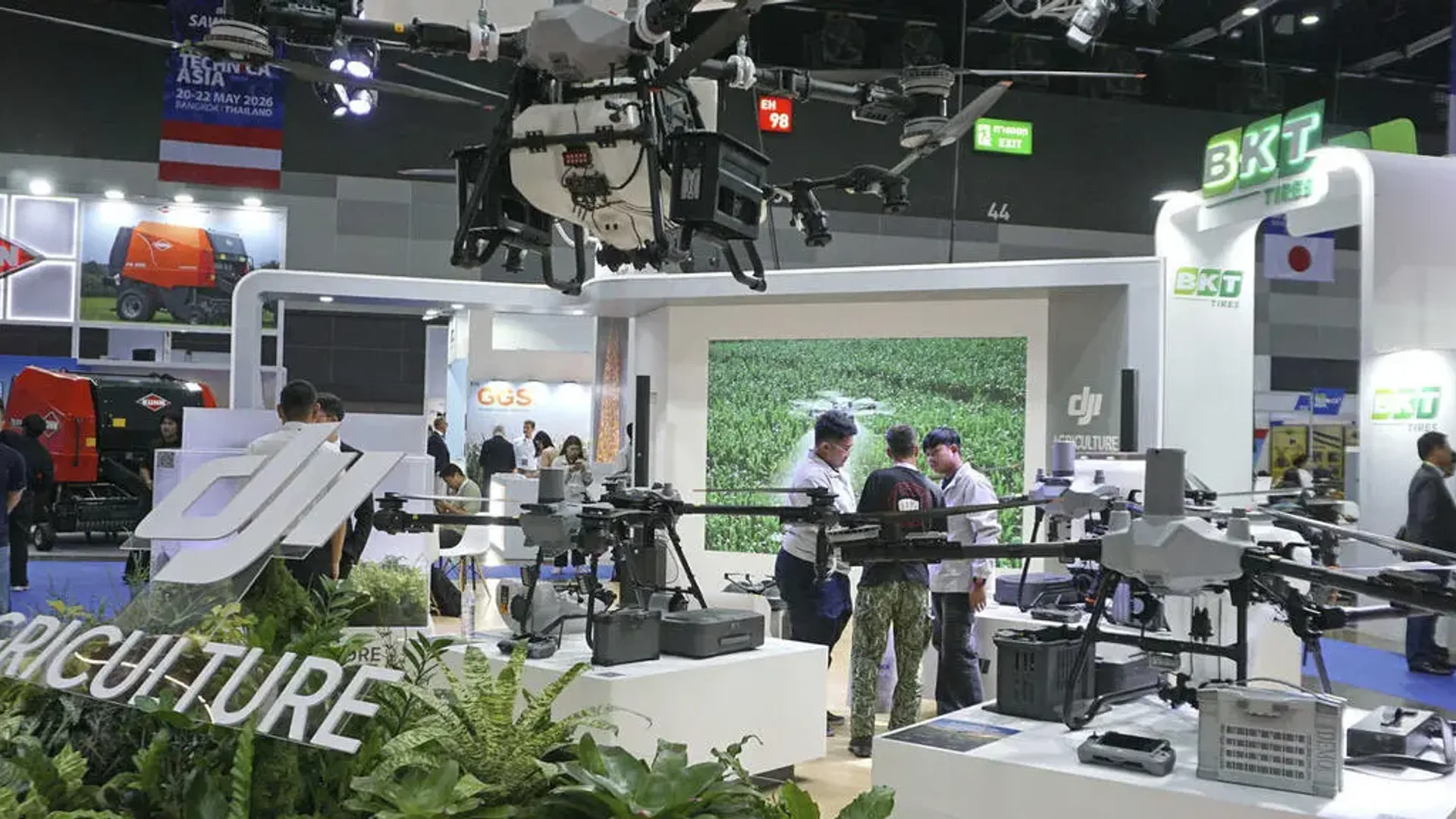 Stand expozițional cu mai multe drone agricole expuse și vizitatori care discută lângă echipamente.