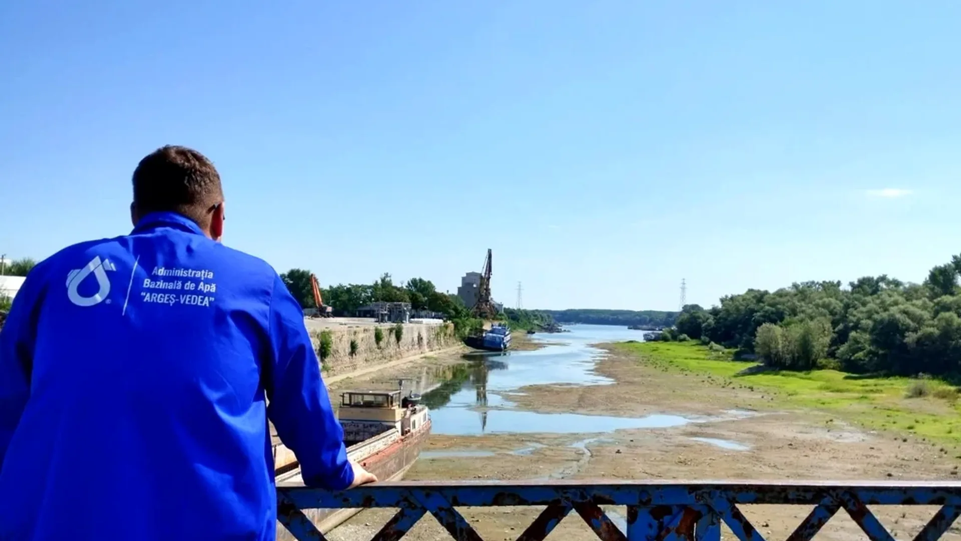 Persoană în jachetă albastră observă albia scăzută de pe pod