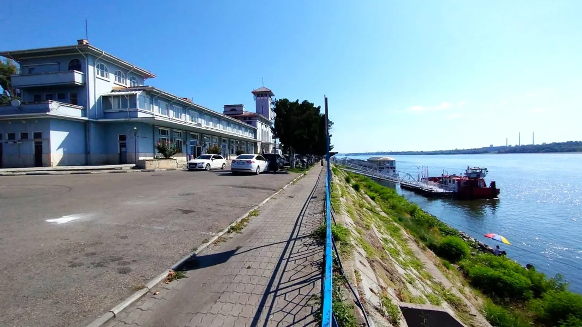 Clădire pe malul Dunării, promenadă și ambarcațiuni pe apă
