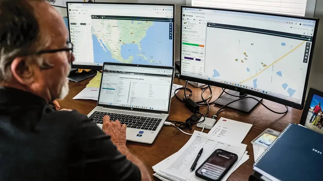 Fermier analizează hărți și date agricole pe laptop și monitoare