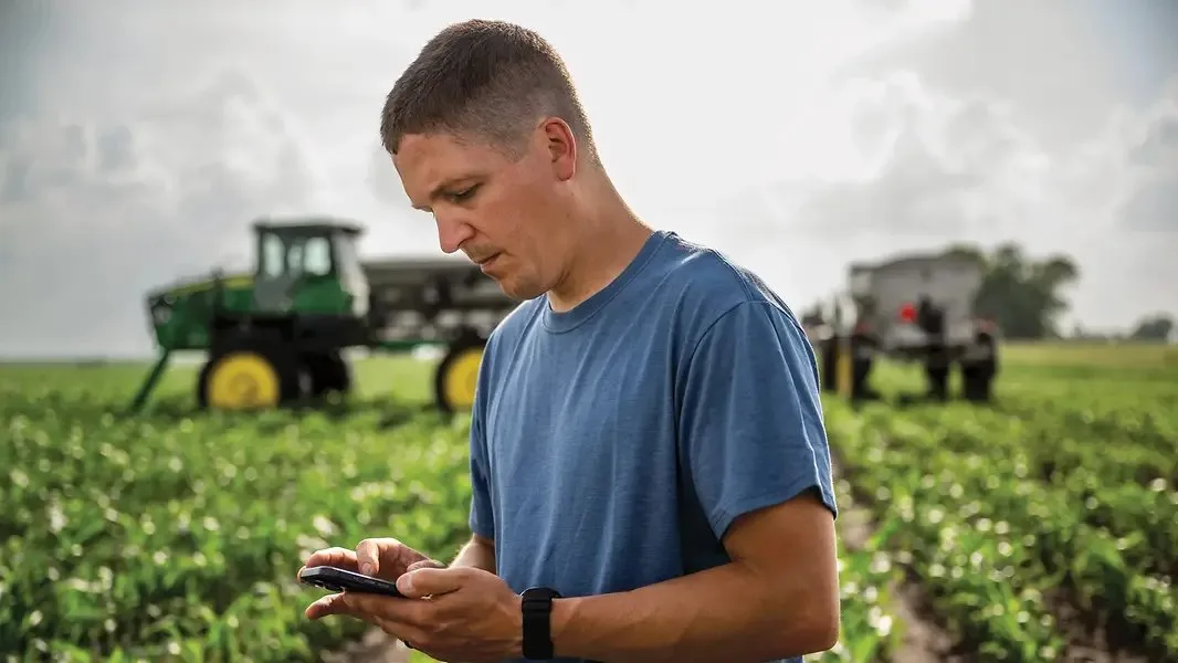 Tânăr fermier folosește telefonul lângă utilaje agricole pe câmp