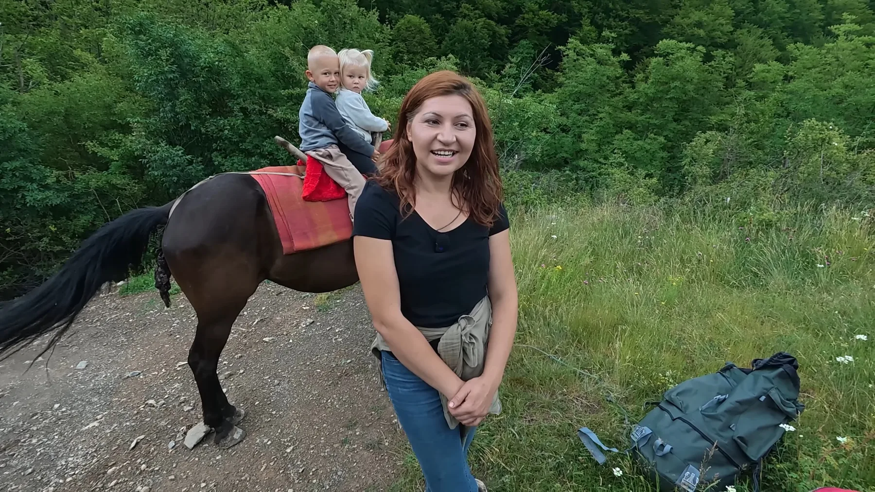 Tânără zâmbind lângă un cal pe care stau doi copii