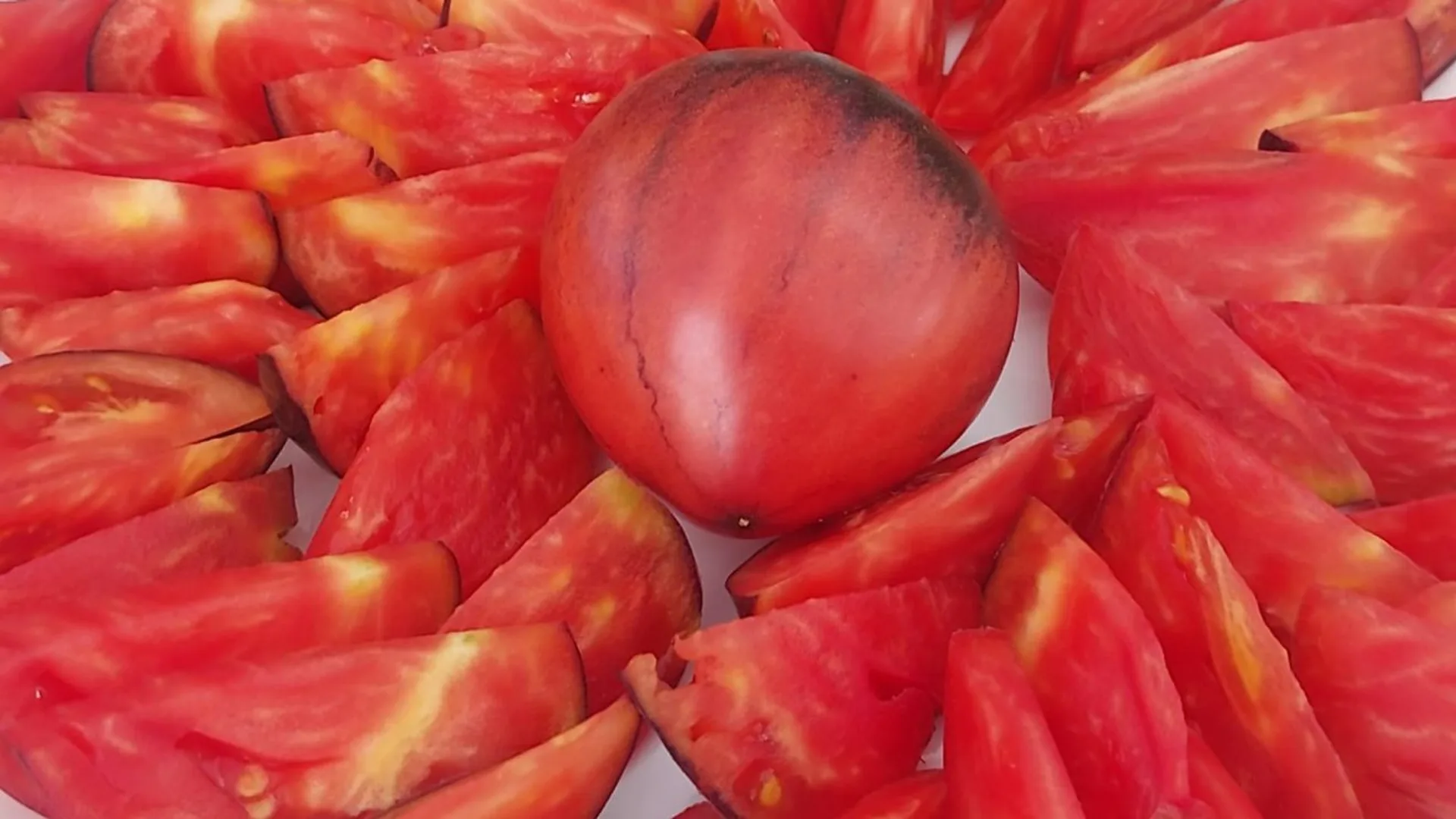 Tomată bicoloră între felii de roșii roșii pe o farfurie