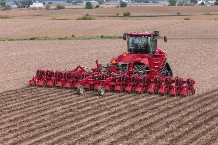 Tractor roșu cu utilaj strip-till lucrând benzi într-un câmp arat