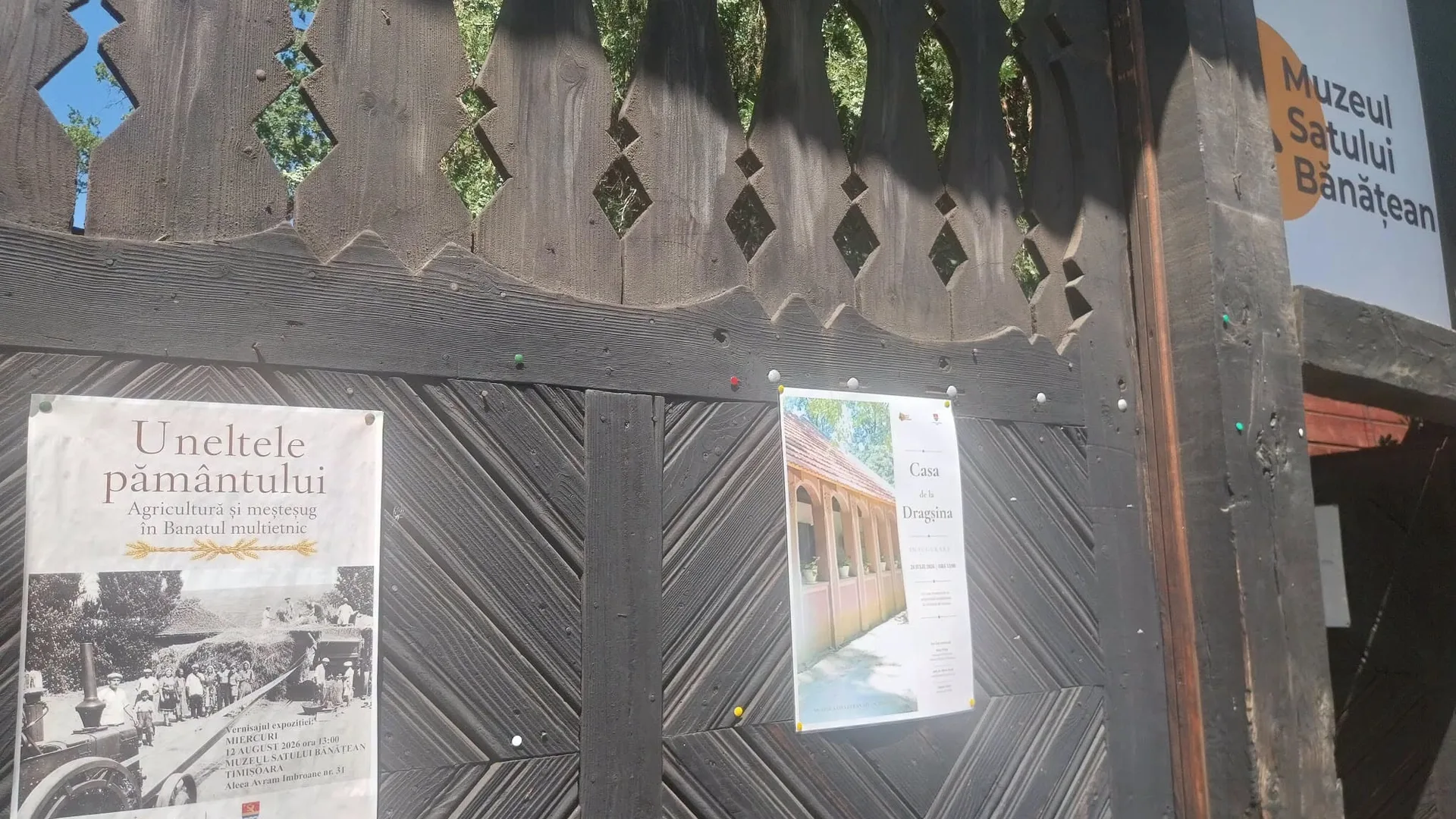 Poartă de lemn a Muzeului Satului Bănățean, cu afișe de expoziție