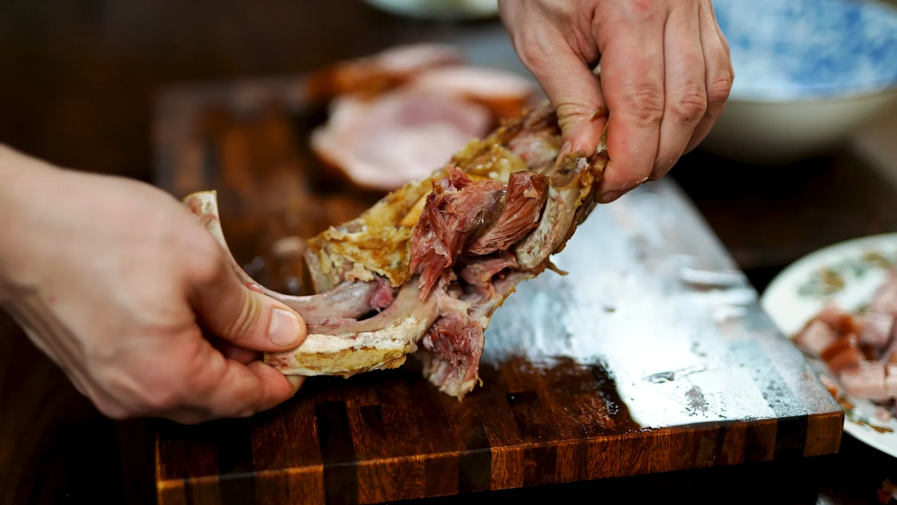Mâini desprinzând carne afumată de pe os, pe tocător