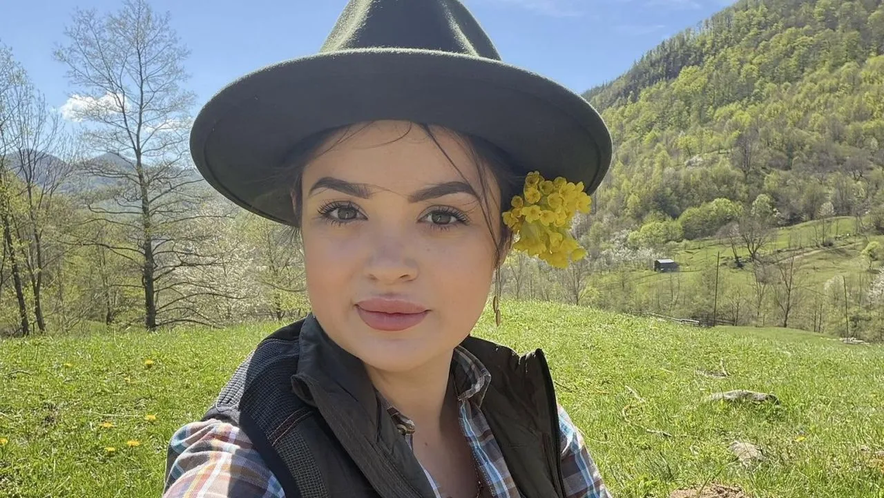 Tânără cu pălărie pe o pajiște montană, ținând flori galbene