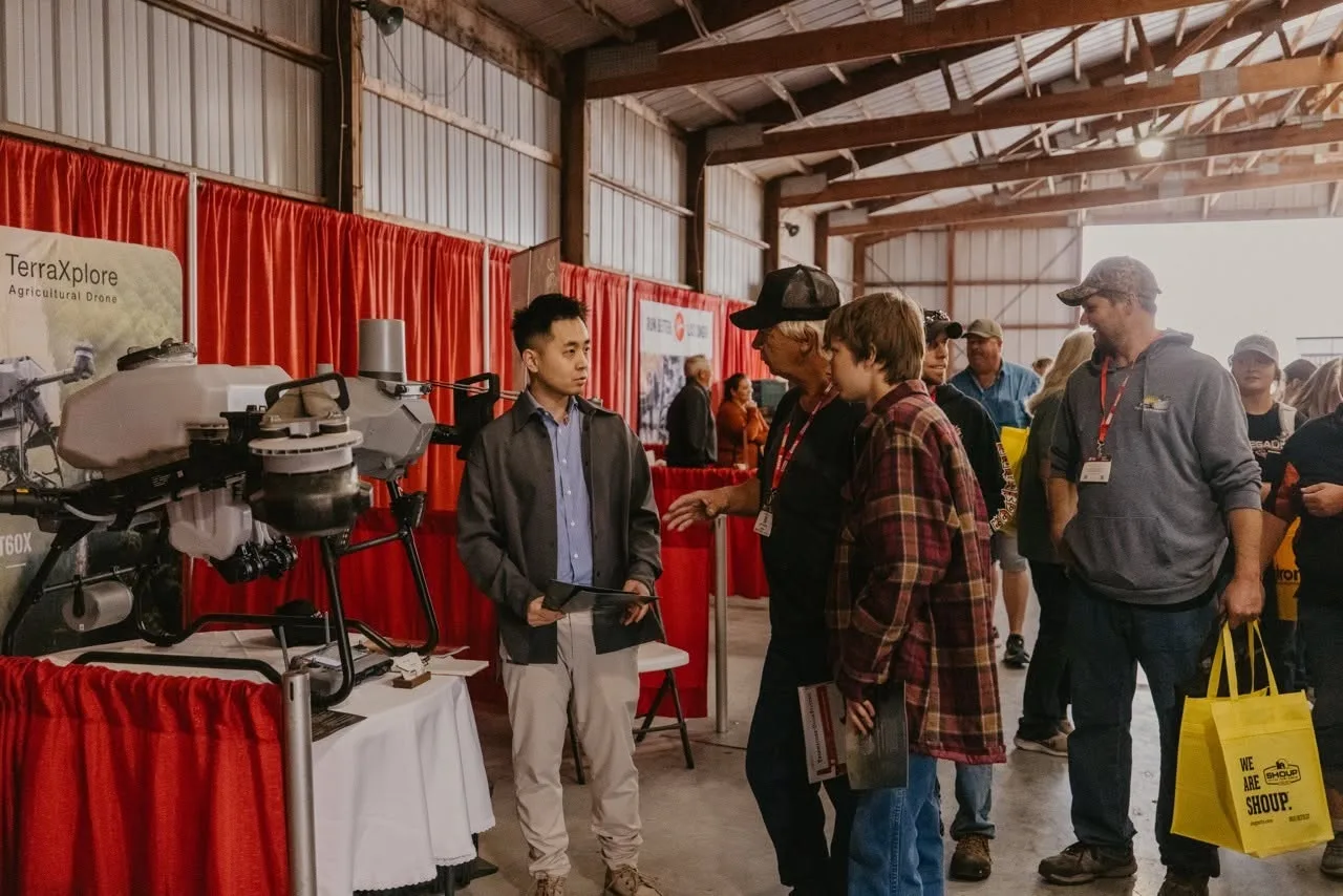 Vizitatori discută cu un expozant lângă o dronă agricolă la stand