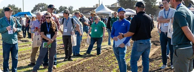 Grup de participanți discută pe teren agricol, lângă standuri de eveniment