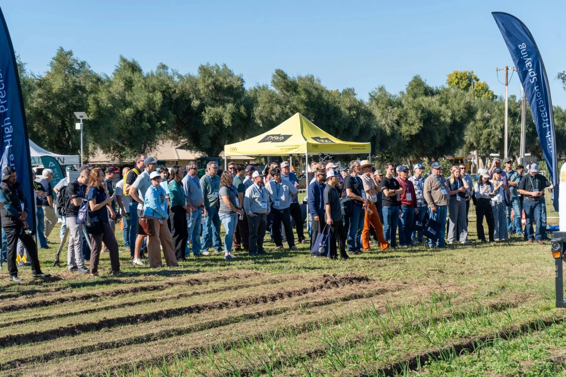 Participanți adunați pe câmp la demonstrație agricolă, lângă corturi și steaguri